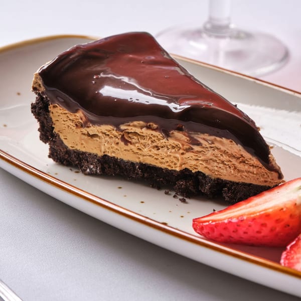 A slice of chocolate peanut butter pie with a chocolate cookie crust and fresh strawberries.