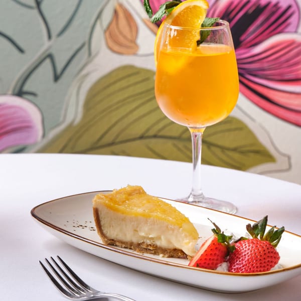 Slice of cheesecake with strawberries and a mimosa on a white table with floral background.