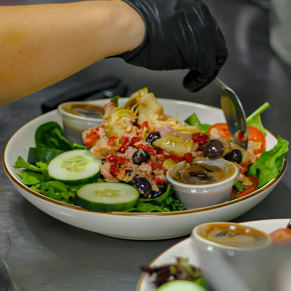 A chef in black gloves prepares a fresh Italian salad with tuna, olives, and artichokes.