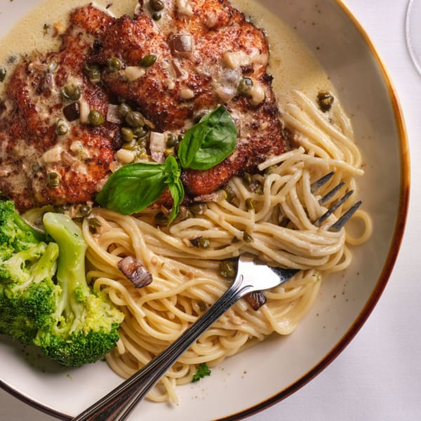 Chicken piccata with capers, basil, spaghetti, and broccoli on a white plate.