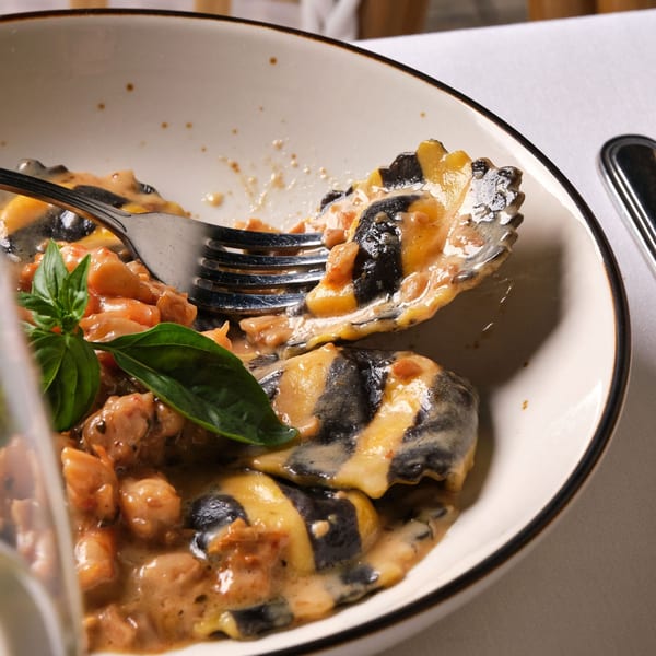 Fork in a bowl of black and yellow ravioli with creamy sauce, chicken, and basil.