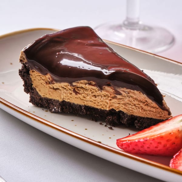 A slice of chocolate peanut butter pie with chocolate ganache and strawberries on a white plate.