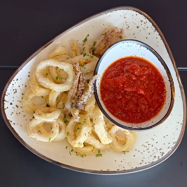 Crispy fried calamari rings and tentacles with a side of red marinara sauce on a white plate.