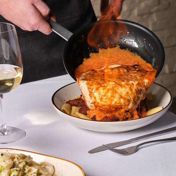 Chef flambéing a dish of chicken parmesan over pasta, served with white wine.