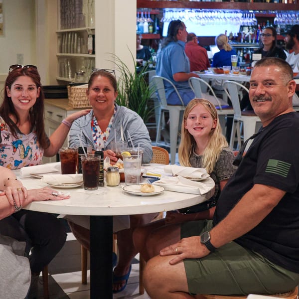 A family of four, including two women, a girl, and a man, smiling at a table in Scarpino's Italian restaurant.
