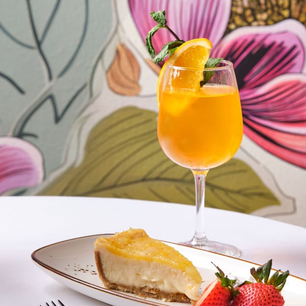 A slice of cheesecake with strawberries and an orange cocktail with mint garnish.