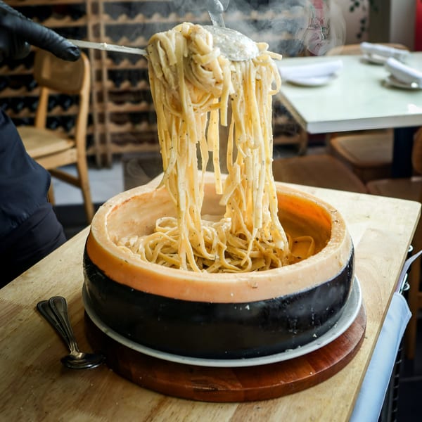 Steaming Scarpino's fettuccine pasta being served from a large Parmesan cheese wheel at a restaurant.