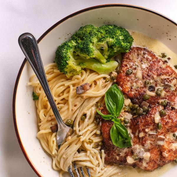 Chicken piccata with capers, creamy spaghetti, and broccoli, garnished with fresh basil.