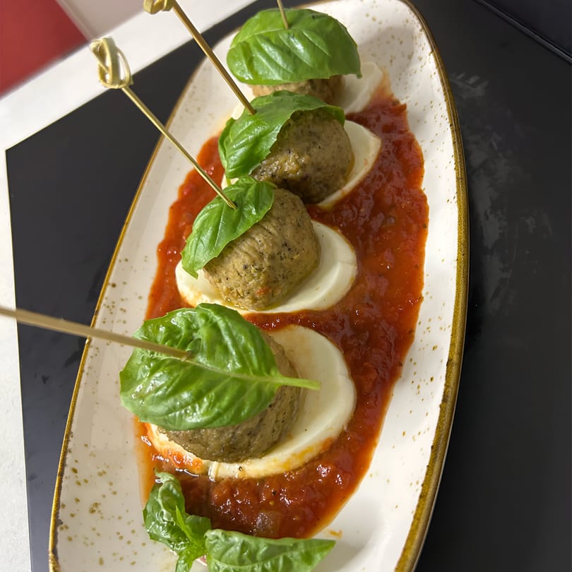 Four meatballs on mozzarella slices with tomato sauce and basil, served on a white plate.