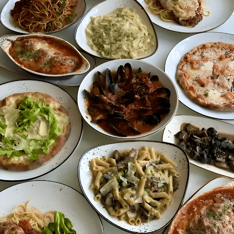 A table filled with various Italian dishes, including pasta, pizza, mussels, and meatballs.