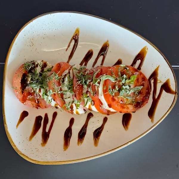 Caprese salad with sliced tomatoes, mozzarella, basil, and balsamic glaze on a white plate.