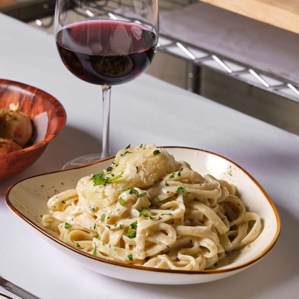 Creamy fettuccine alfredo with parmesan and parsley, a glass of red wine, and bread rolls.
