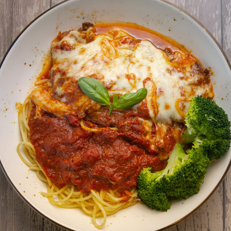 Scarpino's baked spaghetti with melted cheese, marinara, basil, and broccoli on a white plate.