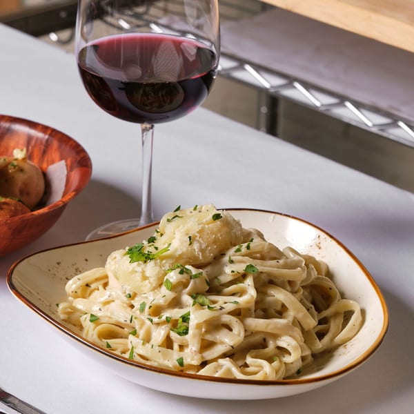 Creamy fettuccine alfredo with parmesan and parsley, a glass of red wine, and bread rolls.